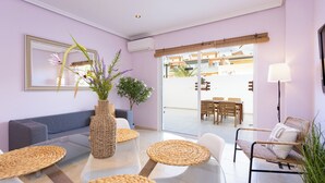 A modern living room with a sofa, a glass coffee table, wicker side tables, a wicker chair, a potted plant, and a large mirror on the wall. - Home2Book Comfy Apt Puertito de Güímar, Pool (Puertito de Güímar)