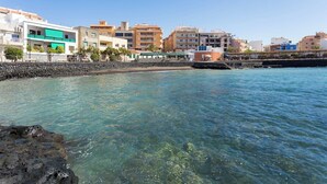 A coastal cityscape with clear blue waters, a stone breakwater, and modern buildings with balconies. - Home2Book Comfy Apt Puertito de Güímar, Pool (Puertito de Güímar)