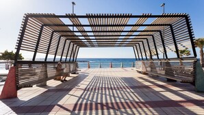 A promenade with wooden benches and a metal pergola structure, overlooking a body of water. - Home2Book Comfy Apt Puertito de Güímar, Pool (Puertito de Güímar)
