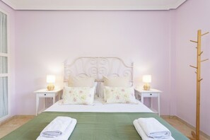 A neatly made bed with floral pillows, two bedside tables with lamps, and a wooden coat rack.