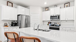 A modern kitchen with white cabinetry, stainless steel appliances, and a central island with two wooden chairs.