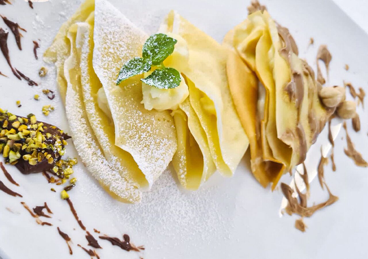 Ein Dessertteller mit Crêpes, Puderzucker, Schokoladensauce und einer Minzblatt-Garnitur.