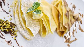 Ein Dessertteller mit Crêpes, Puderzucker, Schokoladensauce und einer Minzblatt-Garnitur.