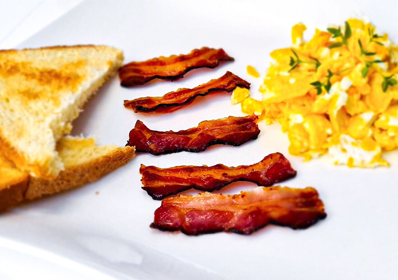A plate with toast, bacon, and scrambled eggs.