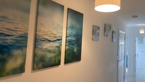Un couloir orné de trois grandes peintures abstraites au mur, d’un luminaire suspendu et d’une porte donnant sur une autre pièce.