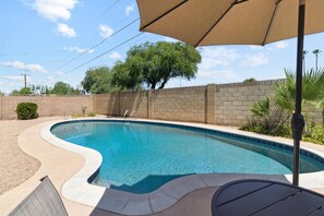 Relax by the pool surrounded by lush greenery and a shaded patio area.