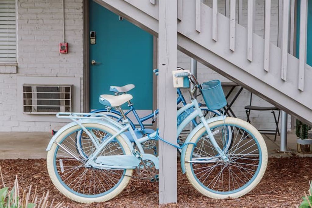 A blue bicycle parked in front of a white building with a teal door.