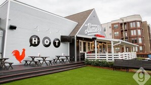 Un bâtiment avec une enseigne indiquant « Lattie B's HOT » et un logo représentant un coq. Il y a des tables à l'extérieur et un espace de repos abrité.