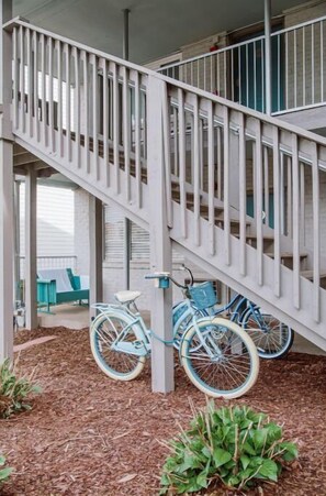 Un escalier avec une rampe blanche mène à un niveau supérieur. Des vélos sont garés au pied de l’escalier.