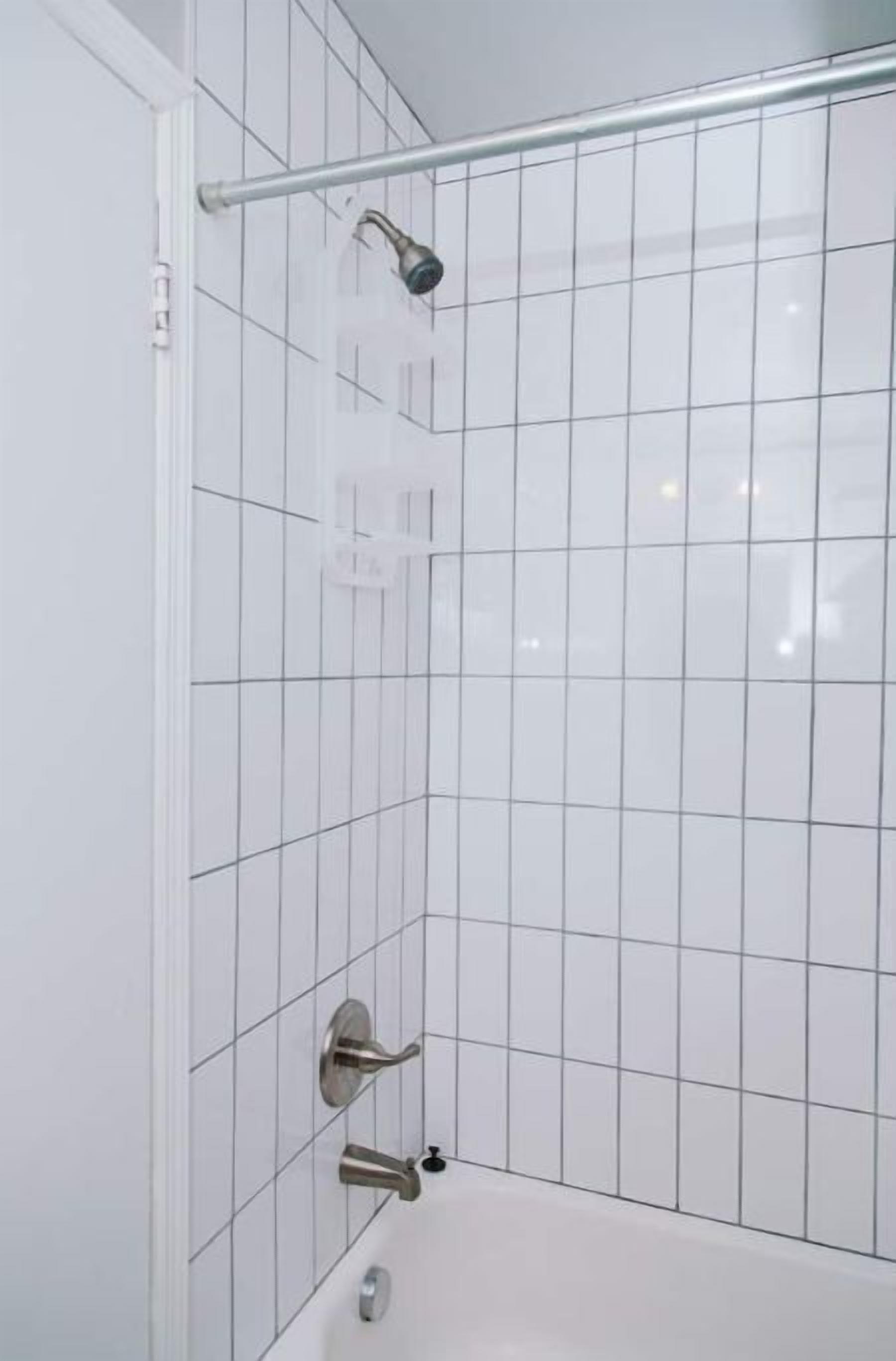 A bathroom with white tiled walls, a shower area, and a bathtub.