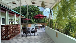 An outdoor patio area with tables and chairs, a covered section, and a view of greenery.