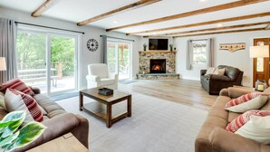 A spacious living room with a fireplace, wooden beams, and large windows.