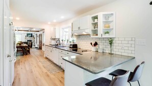 A modern kitchen with white cabinetry, a central island with bar stools, and a dining area with wooden chairs and a table.