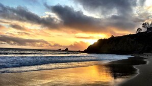Ein Strand mit Sonnenuntergang, Wellen und einer felsigen Klippe.