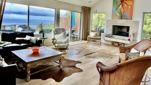 Ein geräumiges Wohnzimmer mit großem Fenster, Kamin und Blick ins Freie.