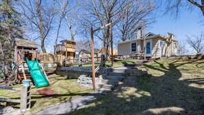 A residential area with a wooden playset, a green slide, and a staircase leading to a house. - Lakefront Family Beach House (Andover)