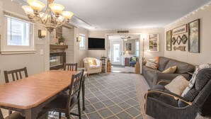 A spacious living room with a dining area, a fireplace, and a kitchen in the background. - Lakefront Family Beach House (Andover)