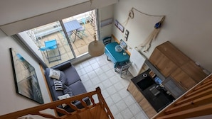 A modern kitchen with a built-in stove, a dining area with a table and chairs, and a living area with a sofa and a large window overlooking a patio. - Duplex near the beach (Les Sables-d'Olonne)
