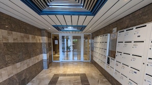 A hallway with a checkered floor, a glass door entrance, and a row of mailboxes on the right. - Duplex near the beach (Les Sables-d'Olonne)