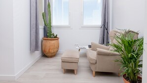 A modern living room with a beige sofa, a small ottoman, a large potted cactus, and a potted plant. - Homey Apt. Cómpeta (Málaga)