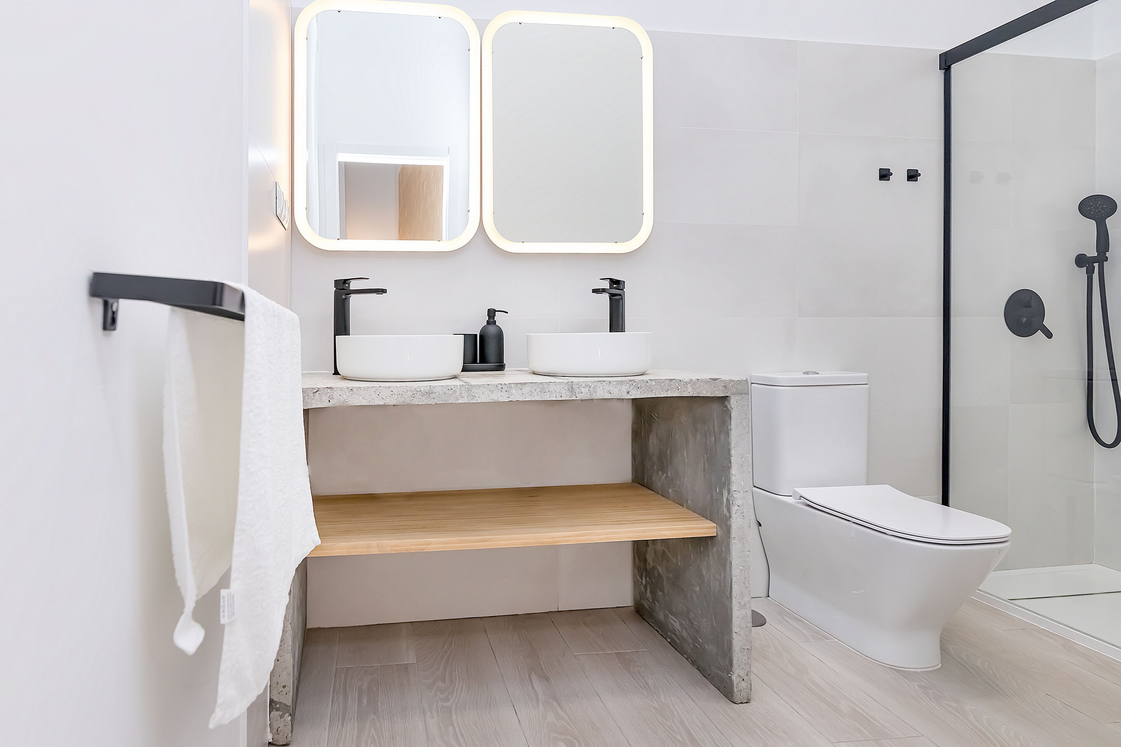Un baño moderno con un lavabo blanco, dos espejos, un inodoro y una zona de ducha.