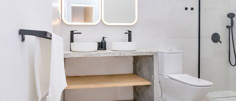 Une salle de bain moderne avec un lavabo blanc, deux miroirs, des toilettes et un espace douche.