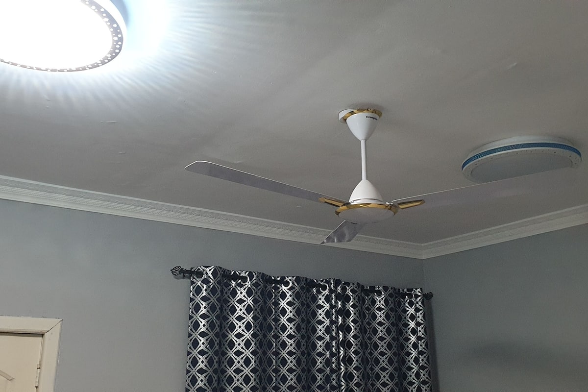 A ceiling fan with a light fixture, a patterned curtain, and a door in a room.