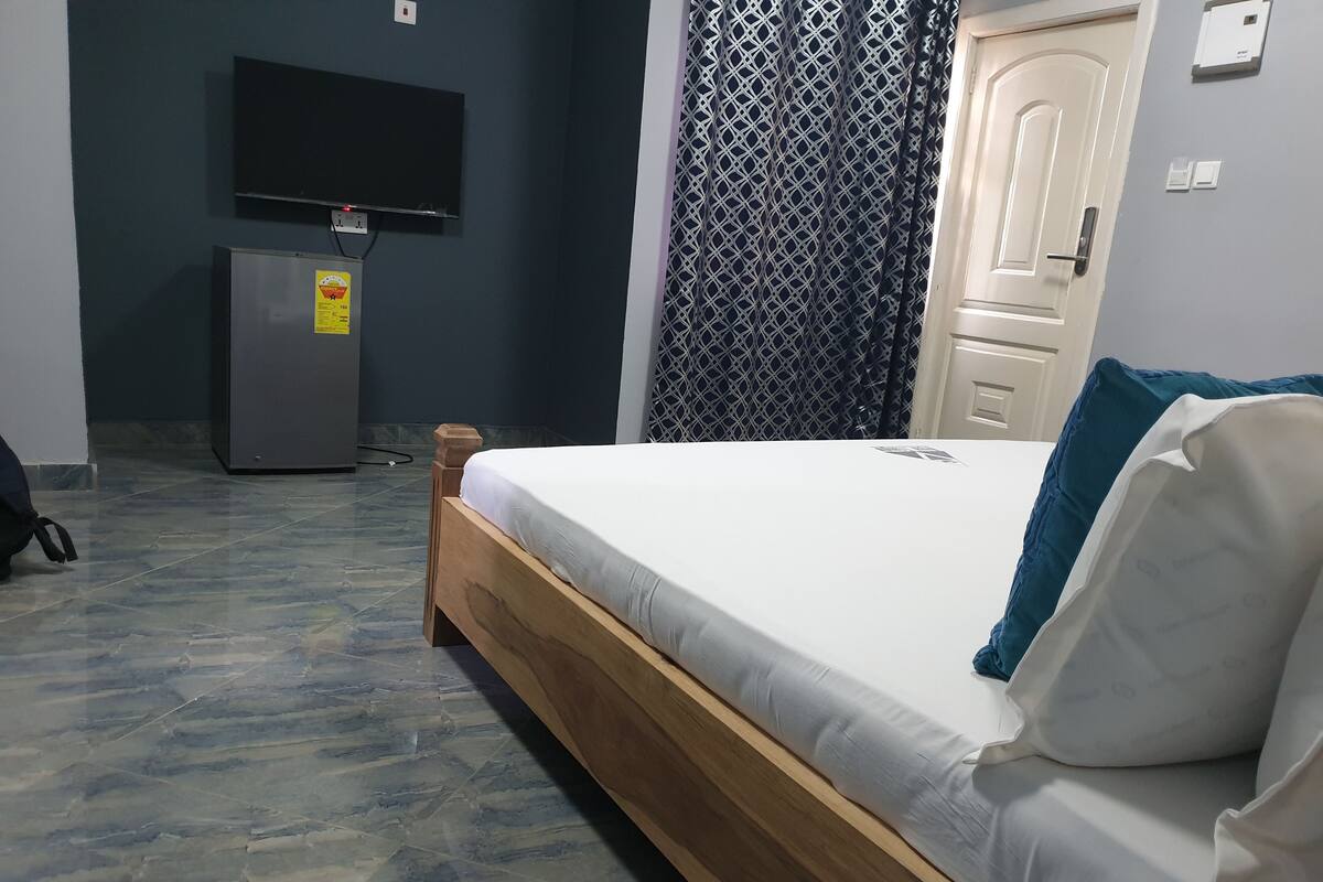 A bedroom with a bed, a television mounted on the wall, a door, and a patterned curtain.
