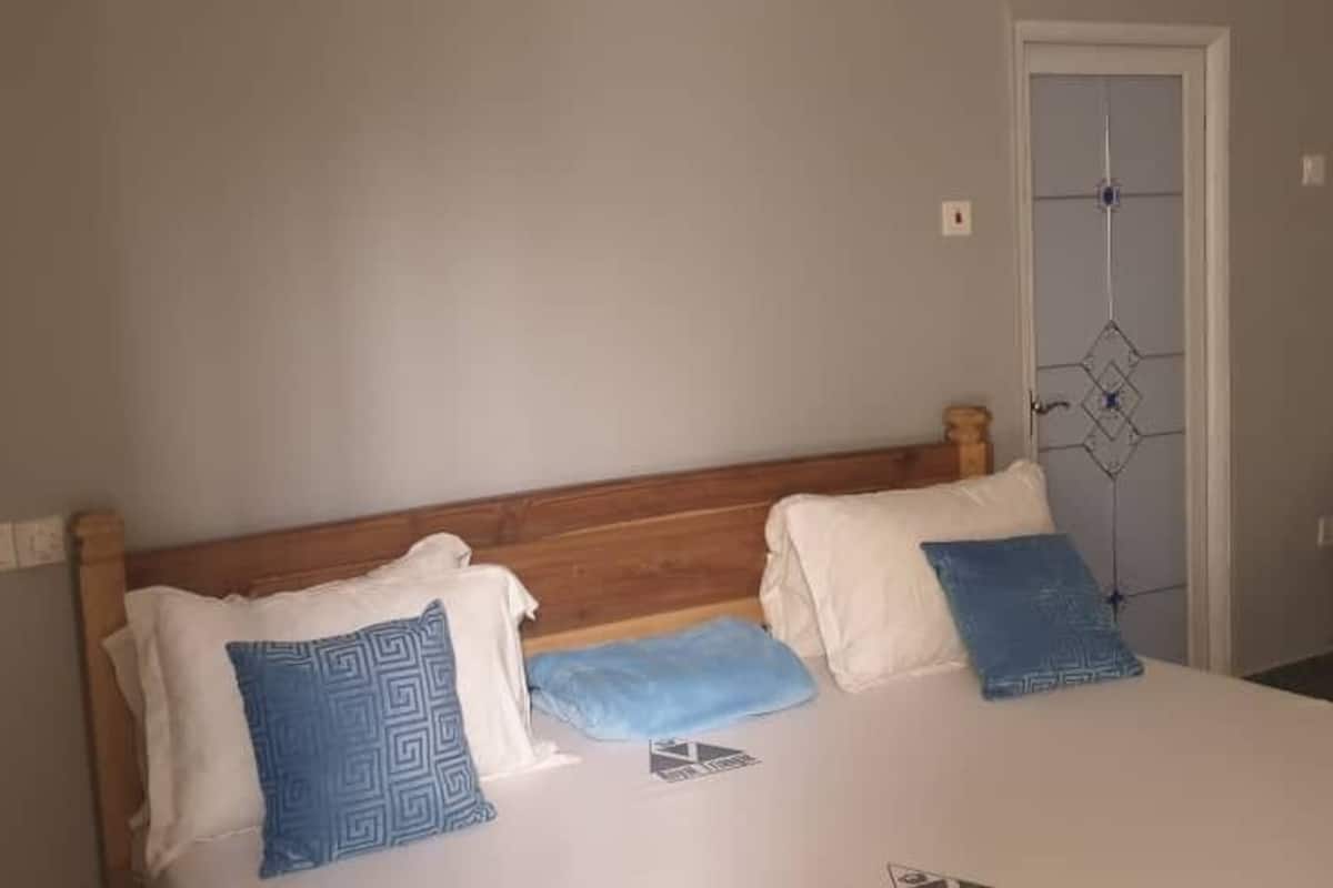 A bedroom with a wooden headboard, a bed with white bedding and two blue patterned pillows, a door with a geometric design, and a chair in the corner.