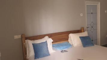Une chambre à coucher avec une tête de lit en bois, un lit recouvert d’une literie blanche et agrémenté de deux coussins à motifs bleus, une porte ornée d’un motif géométrique et une chaise placée dans un coin.