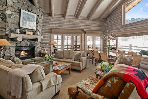 A cozy log cabin interior with a stone fireplace, comfortable seating, and a view of the snowy landscape.