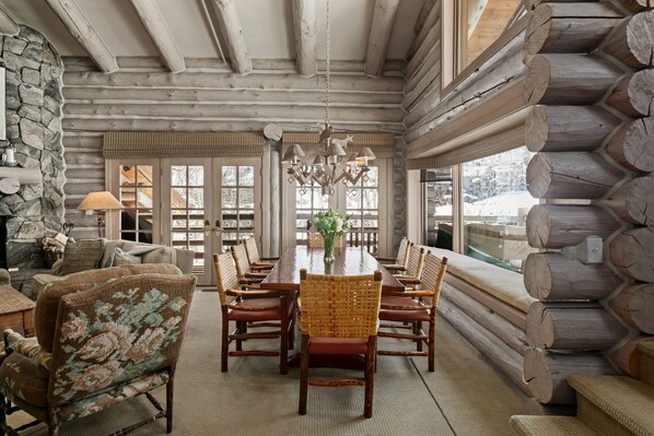 A log cabin interior with a dining table surrounded by chairs, a chandelier, and a stone wall.