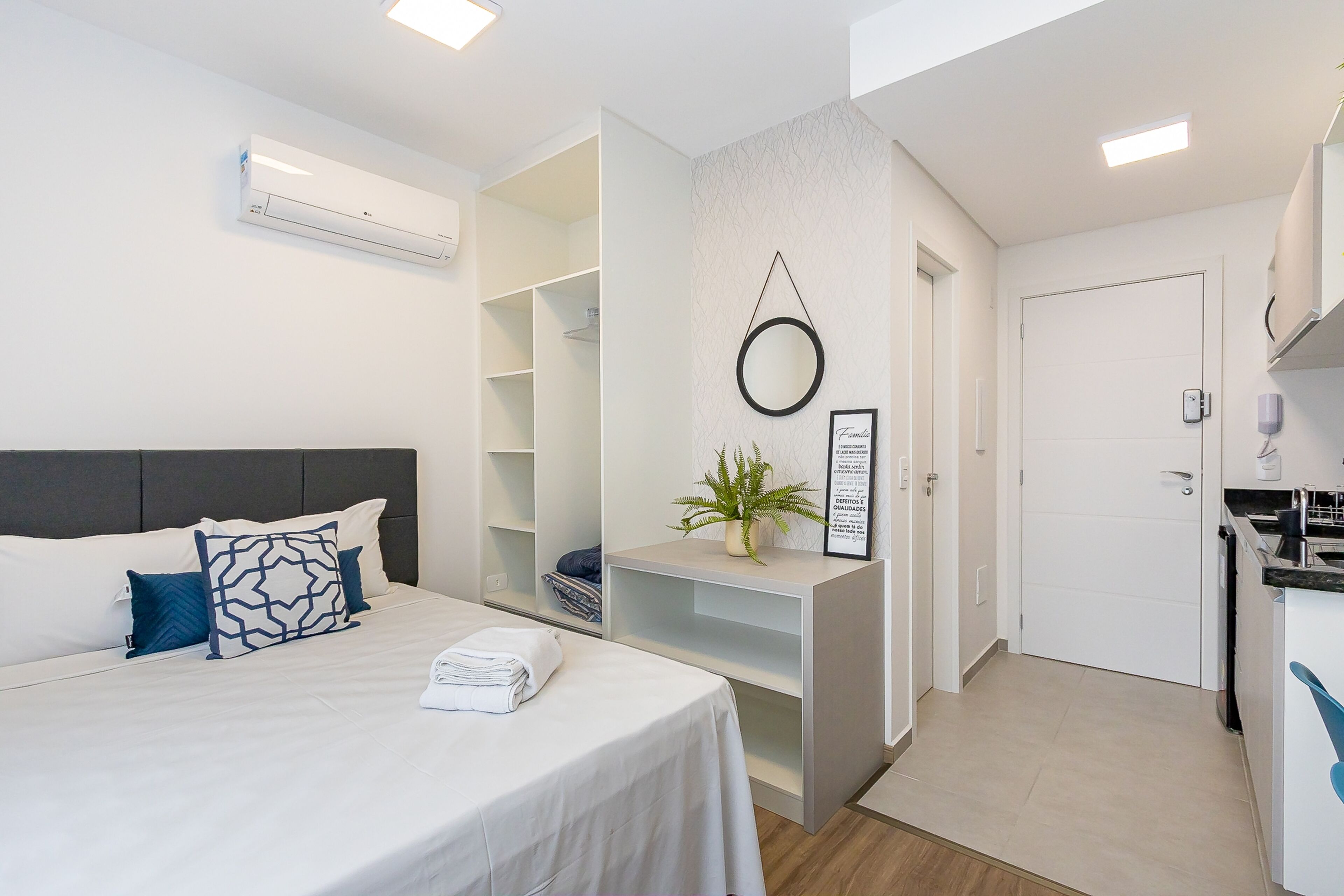 A modern hotel room with a bed, a small kitchenette, a built-in wardrobe, and a bathroom.
