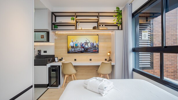 Habitació d'hotel moderna amb un llit, un escriptori, dues cadires, una televisió i vista a l'exterior.