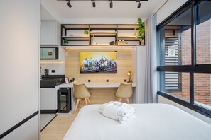 Una habitación de hotel moderna con una cama, un escritorio, dos sillas, un televisor y vistas al exterior.