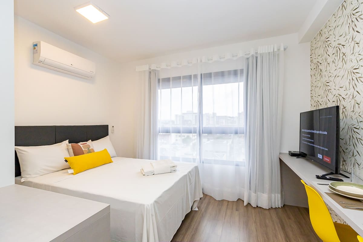 A hotel room with a bed, a TV, and a window with curtains.