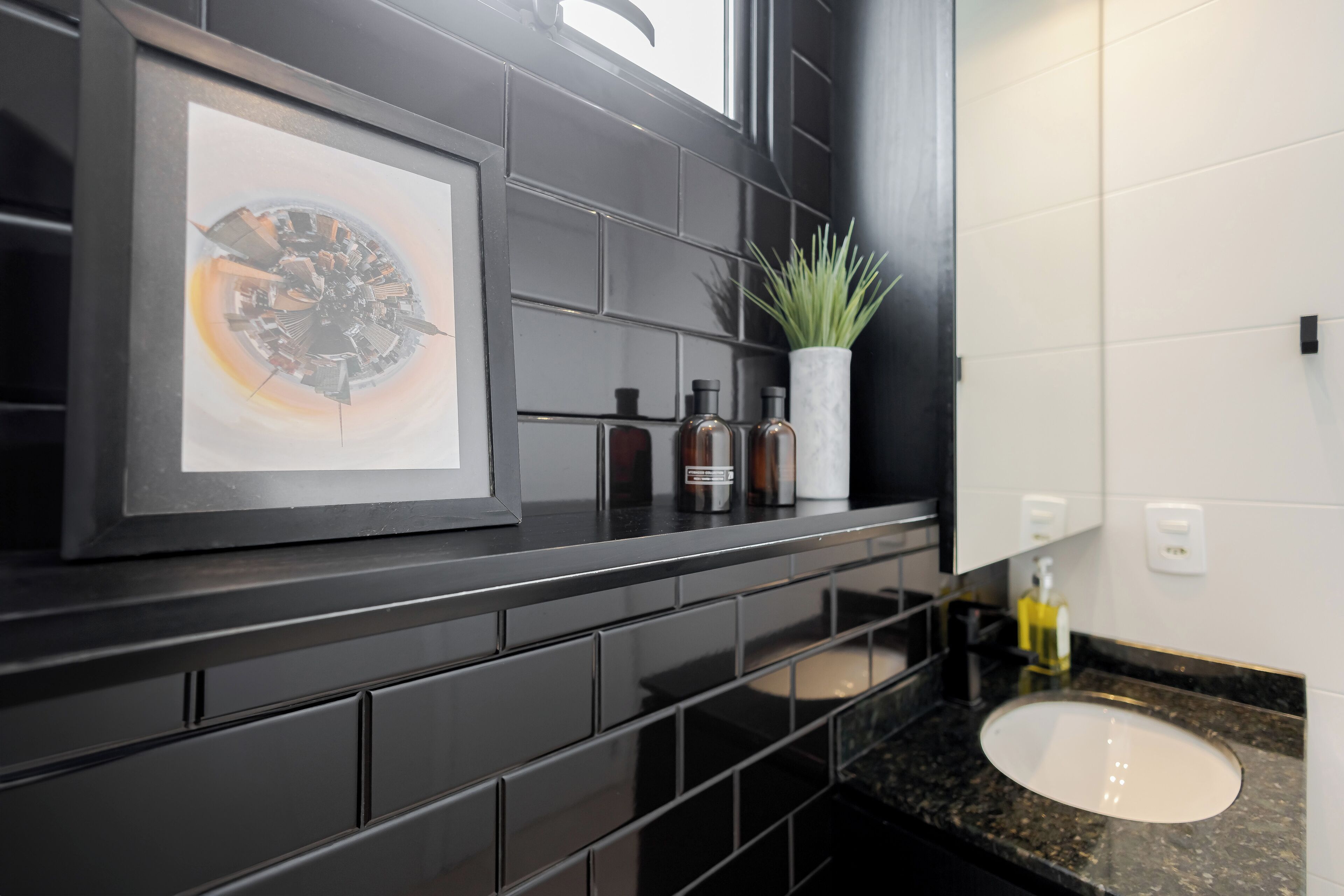 A modern bathroom with a black tiled backsplash, a framed artwork, a potted plant, and a sink with a marble countertop.