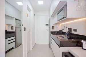 Una cocina moderna con armarios blancos, un refrigerador de acero inoxidable, una encimera negra y un horno empotrado.