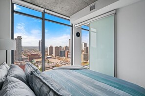 A bedroom with a large window, a bed with pillows, and a view of a cityscape. - DT Views |King Bed |Mins to Stampede | UG Parking (Calgary)
