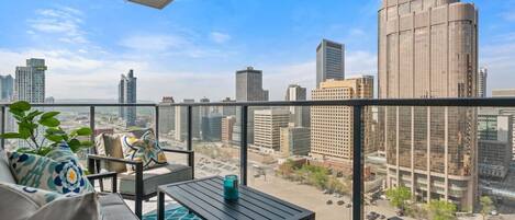A balcony with a city view, a table, chairs, and a potted plant.