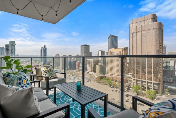 Varanda com vista para a cidade, uma mesa, cadeiras e um vaso com planta.