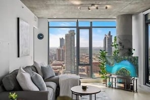Uma sala de estar moderna com uma janela grande, um sofá, uma mesa de centro e um quadro de uma paisagem.