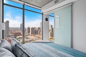 Quarto com uma janela grande, uma cama e vista para a paisagem urbana.