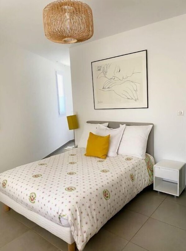A bedroom with a bed, a bedside table, a lamp, and a wall-mounted artwork.