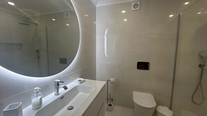 Een moderne badkamer met een grote spiegel, een wastafel met zeepdispenser, een toilet en een douchegedeelte.