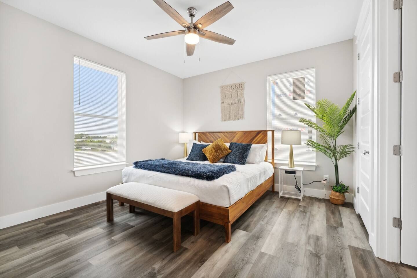 Une chambre avec un lit en bois, un banc, un ventilateur de plafond et une plante en pot.