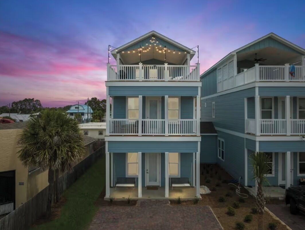 A two-story residential building with a balcony on the upper floor, a covered front porch, and a small front yard.
