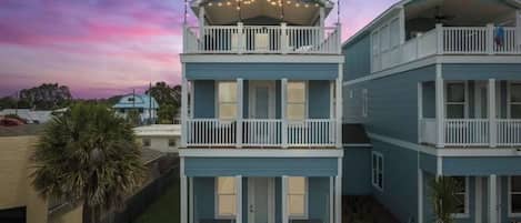 A two-story residential building with a balcony on the upper floor, a covered front porch, and a small front yard.