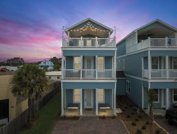 A two-story residential building with a balcony on the upper floor, a covered front porch, and a small front yard.