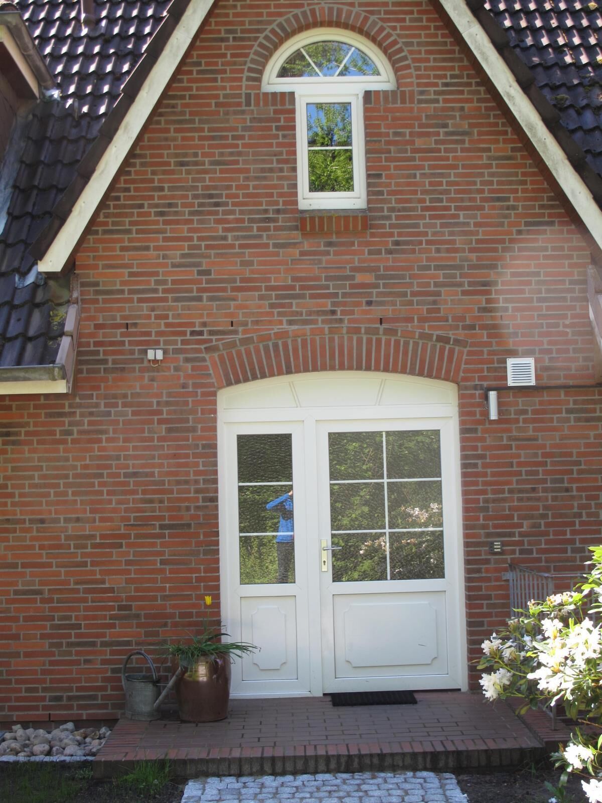 A brick house with a white double door, a small window above the door, and a brick pathway leading to the entrance.